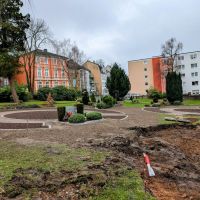Auf einer Friedhofsfläche sind angelegte Kreise mit vorbereiteten Beeten. Die Beetstruktur ist schon angelegt und die Erde vorbereitet, eine Bepflanzung fehlt noch. In der unteren rechten Bildecke ist eine ausgehobene Vertiefung und freigelegte Erde.