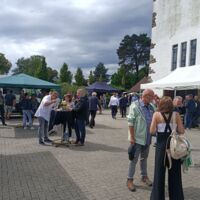 Menschen stehen auf einem Fest in kleinen Grüppchen und quatschen, essen und trinken.